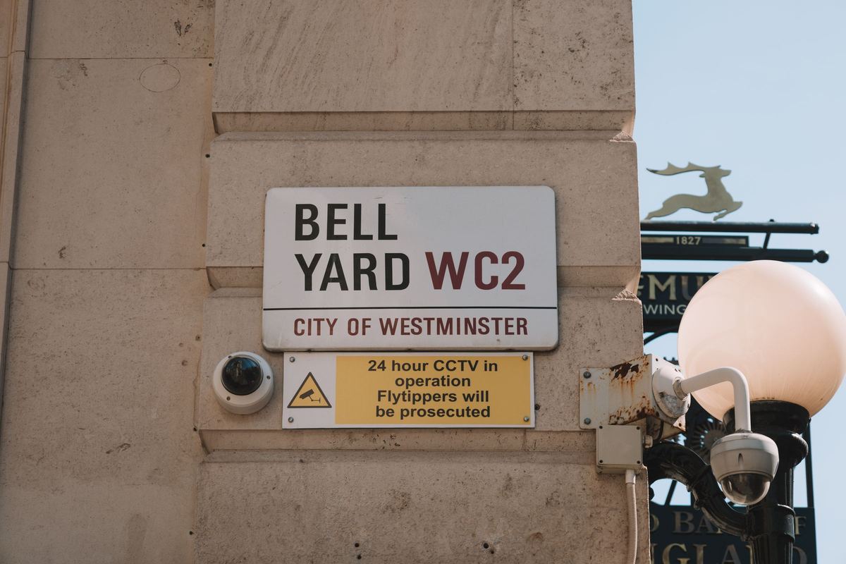 CCTV cameras and a "24 hour CCTV in operation" notice beneath the Bell Yard street sign in the City of Westminster, London.