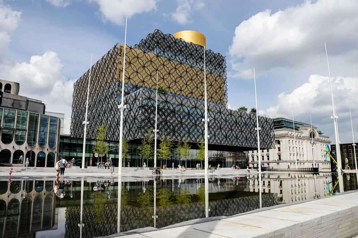 The Library of Birmingham with its gold and filigree facade reflected in water in Centenary Square.