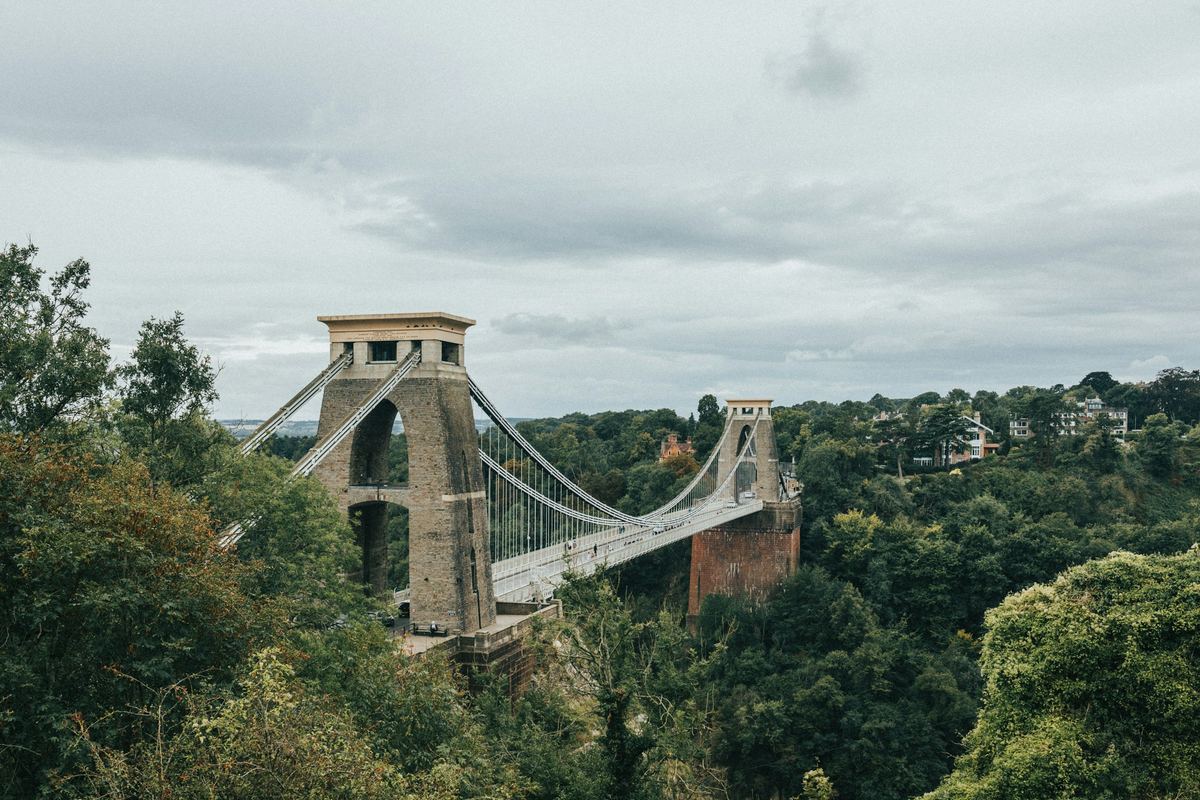 The Clifton Suspension Bridge spanning the wooded Avon Gorge in Bristol under a grey sky.