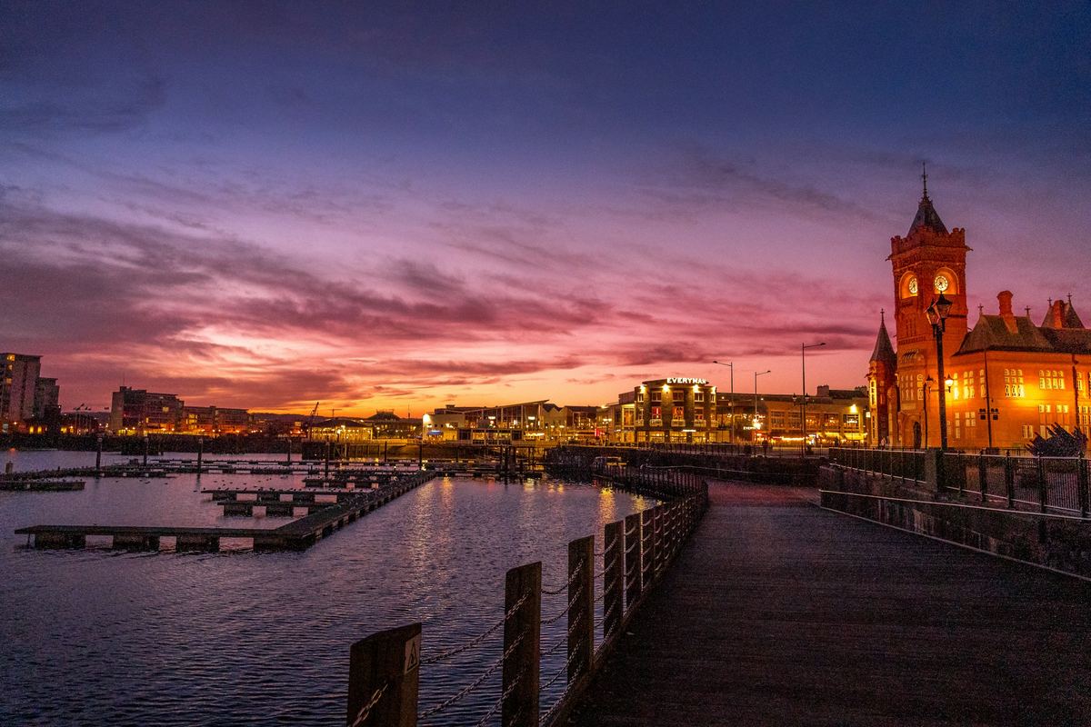 Cardiff Bay boardwalk at sunset with the illuminated red-brick Pierhead Building.