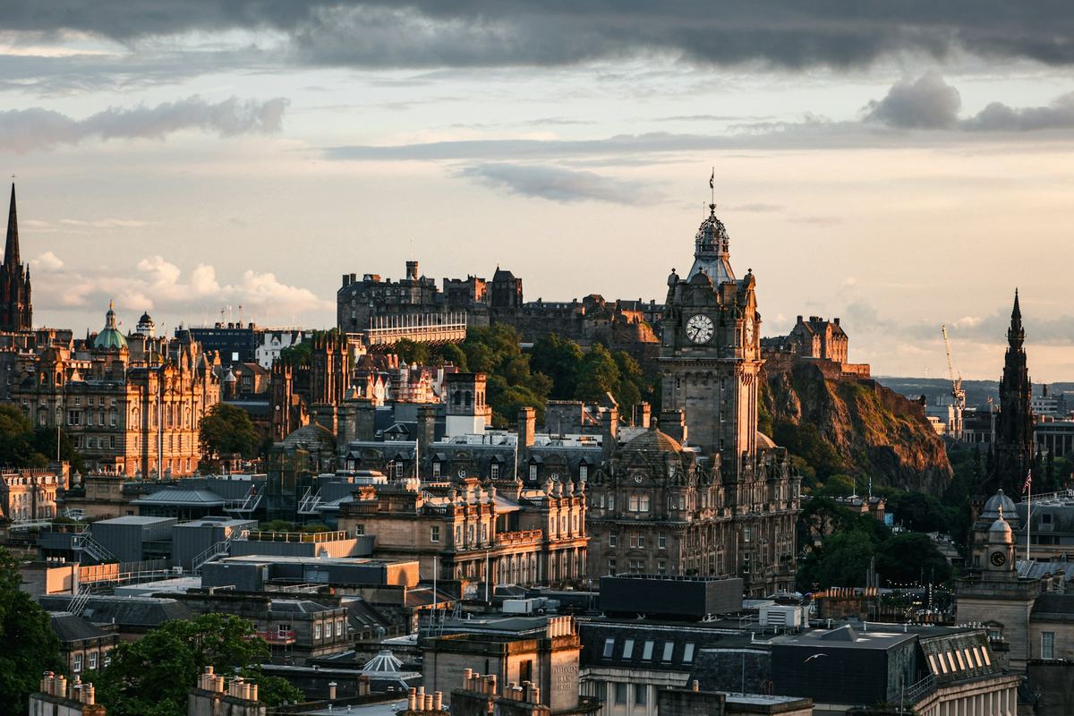 Edinburgh rooftops with the Balmoral clock tower and Edinburgh Castle in warm evening light.