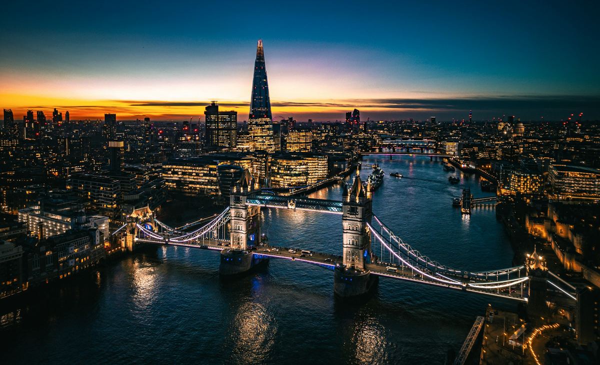 Aerial night view of Tower Bridge lit up over the Thames with the Shard behind at sunset.