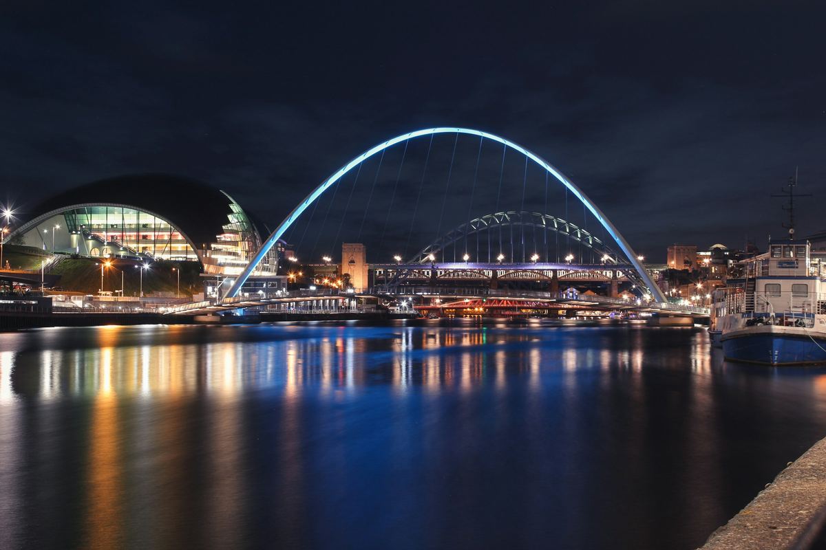 The Gateshead Millennium Bridge, Tyne Bridge and Sage Gateshead lit up over the River Tyne at night.