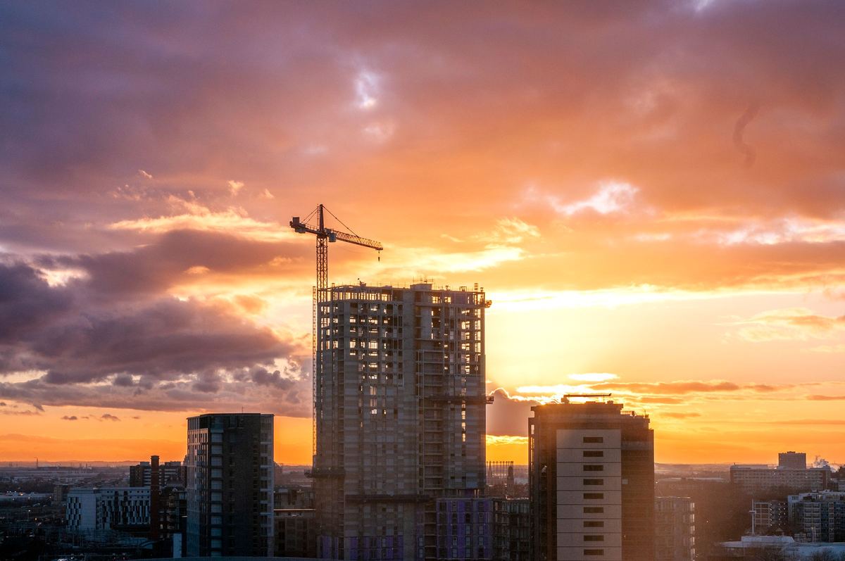 A tower crane above a high-rise building under construction in Manchester at sunset.