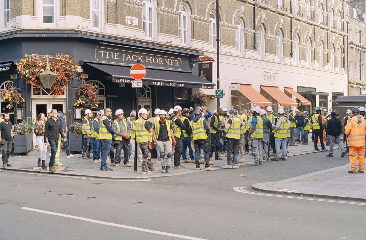 A large group of construction workers in hi-vis vests and hard hats gathered on a London street.