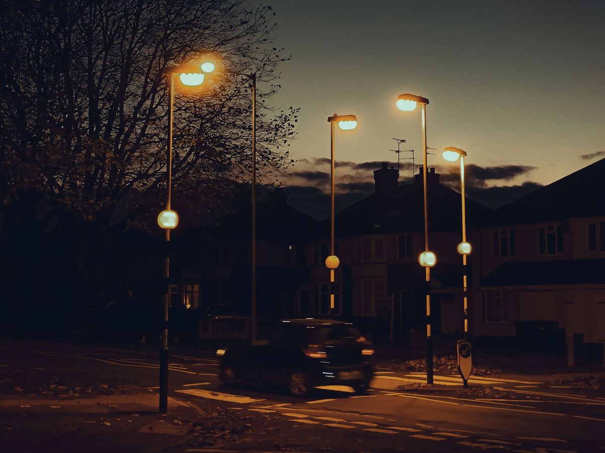 A residential street in England at night, lit by streetlights, with a car at a zebra crossing.
