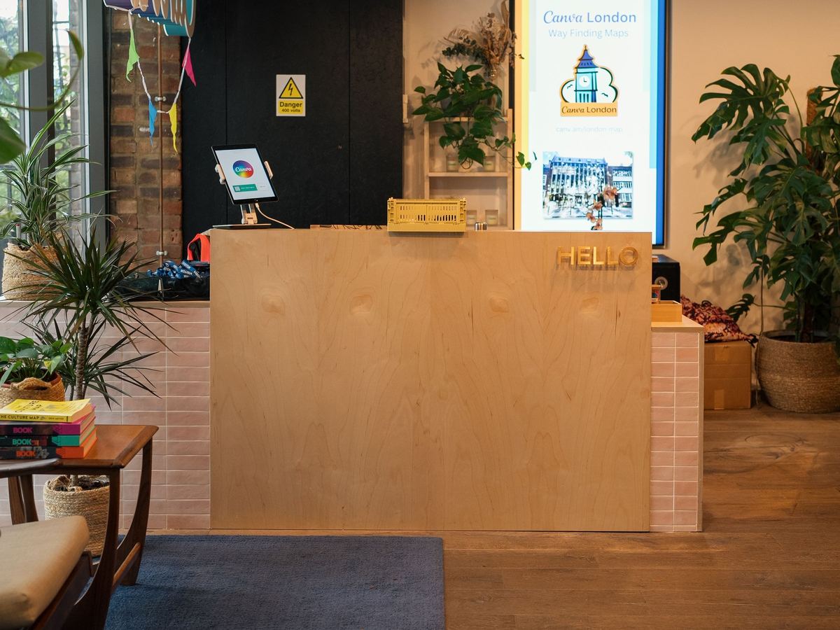 The reception desk of a modern office in London, with plants and a welcome screen.