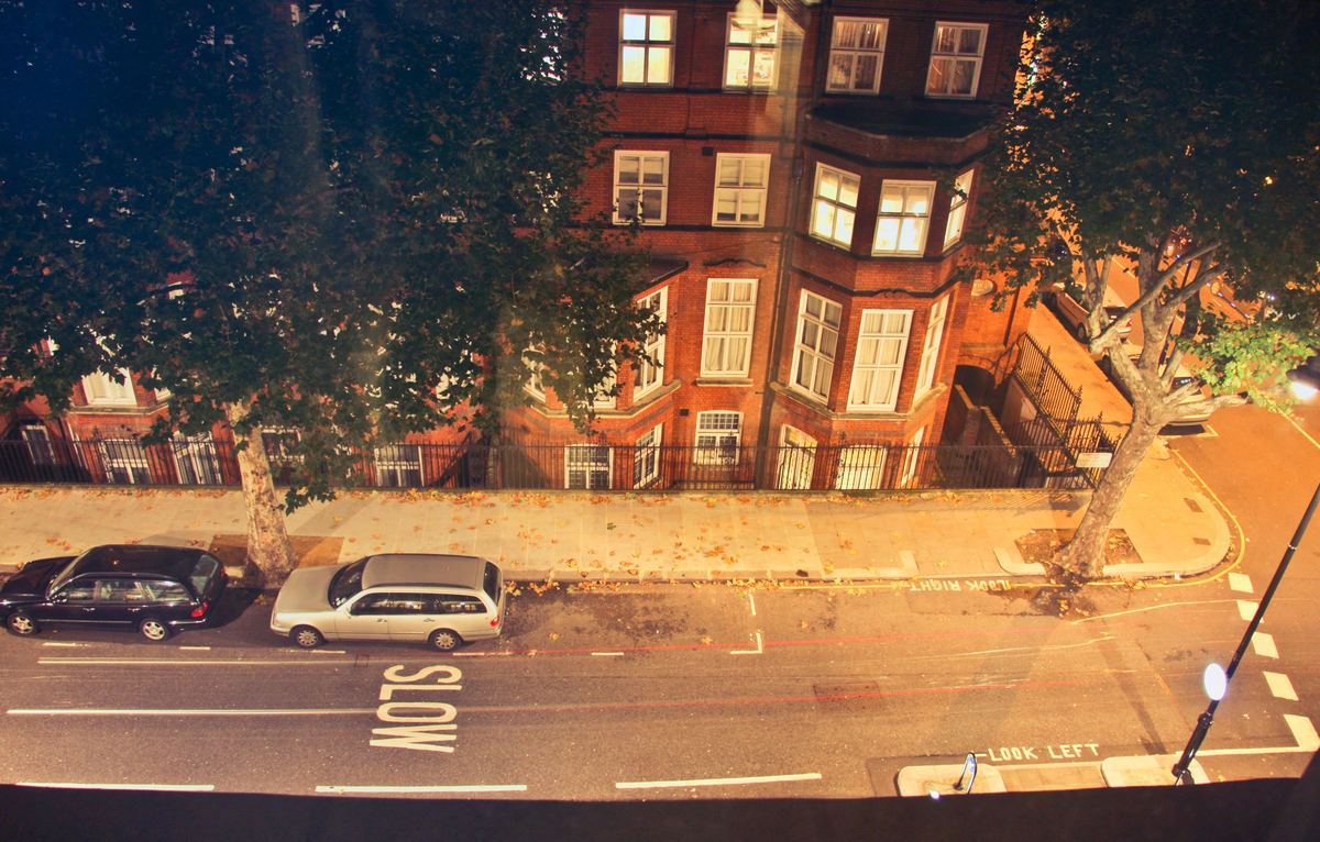 A London street at night seen from above, with cars parked outside a red-brick building.