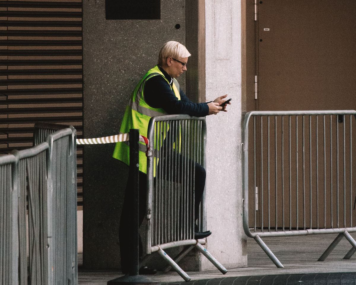A security officer in a hi-vis vest stands at crowd barriers outside a building in London.
